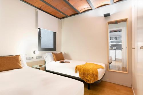 Habitación con 2 camas y espejo. en Aspasios Las Ramblas Apartments, en Barcelona