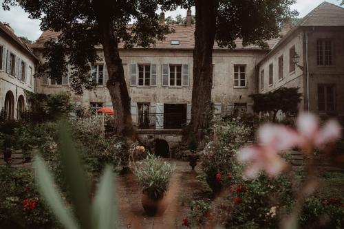 un jardin fleuri et un bâtiment avec un arbre dans l'établissement La Fontaine Racine - Chambres d'hôtes, à La Ferté-Milon