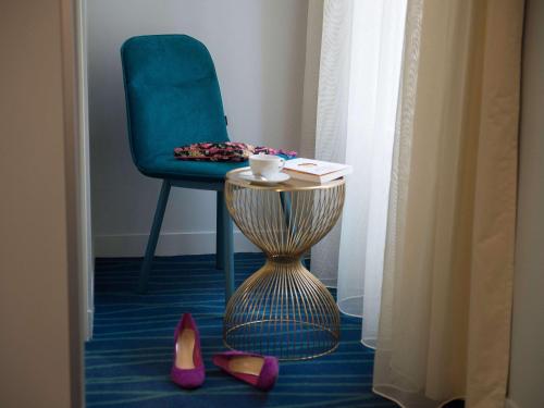 um quarto com uma cadeira azul, uma mesa e sapatos em Hôtel Mercure Paris Suresnes Longchamp em Suresnes