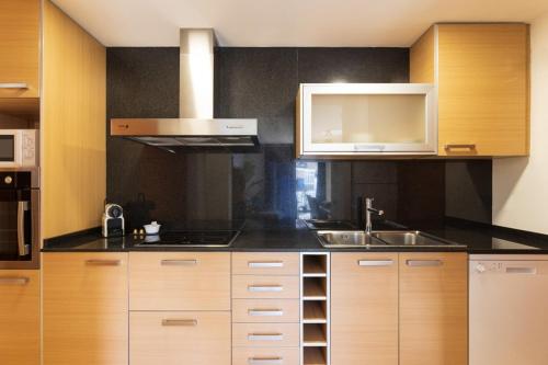 a kitchen with wooden cabinets and a sink and a microwave at Lucas House Apartments by Sitges Group in Sitges
