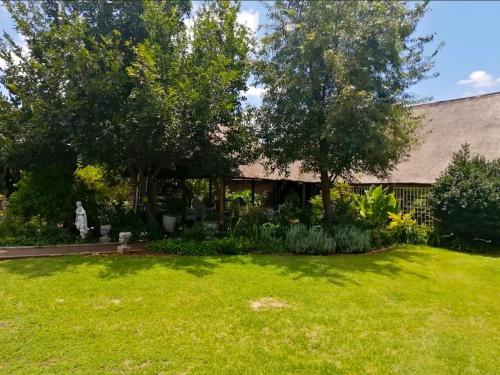 Midvaal Guesthouse في Meyerton: ساحة بها عشب أخضر وأشجار ومنزل