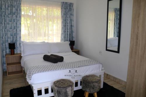 Un dormitorio con una cama blanca con dos taburetes y una ventana en Relaxing Mountain FarmStay w hikes, boma, pool, en Magaliesburg