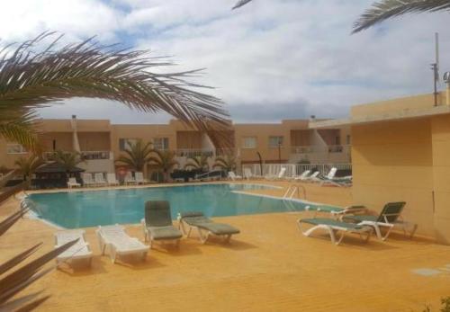 Una piscina en un hotel con sillas y una palmera. en Mi casa su casa, en Caleta de Fuste