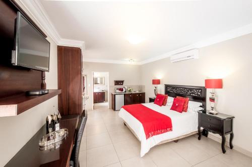 a bedroom with a bed with red pillows and a television at Adato Guesthouse in Potchefstroom
