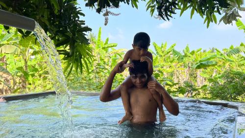 a man with a child on his shoulders in a swimming pool at SERENE Stays - Kjsb farmhouse THANJAVUR in Thanjāvūr