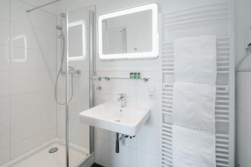 a white bathroom with a sink and a shower at Hotel am Denkmal Norderney in Norderney