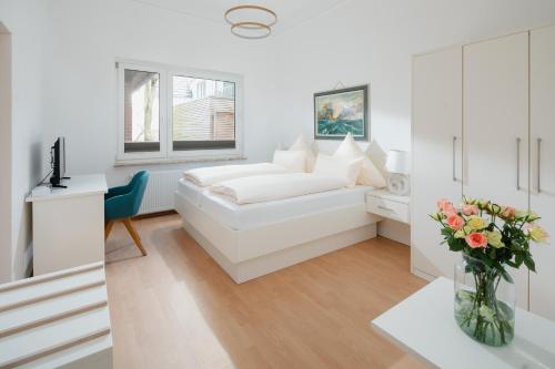 a white bedroom with a bed and a vase of flowers at Hotel am Denkmal Norderney in Norderney
