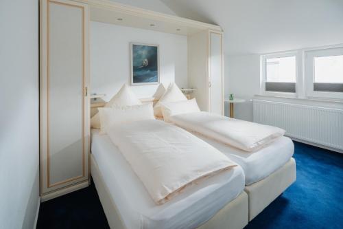 two beds in a room with white sheets and pillows at Hotel am Denkmal Norderney in Norderney