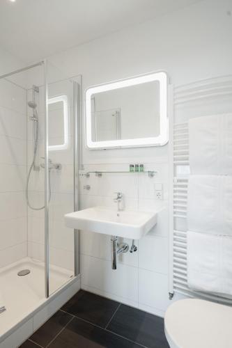 a white bathroom with a sink and a shower at Hotel am Denkmal Norderney in Norderney
