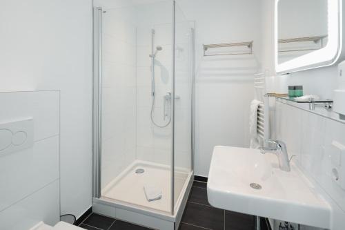 a white bathroom with a shower and a sink at Hotel am Denkmal Norderney in Norderney