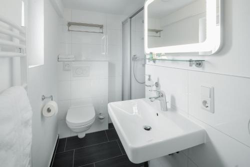 a white bathroom with a sink and a toilet at Hotel am Denkmal Norderney in Norderney