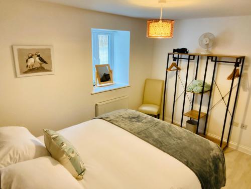 ein Schlafzimmer mit einem Bett, einem Fenster und einem Stuhl in der Unterkunft Above the Bay - Enclosed garden apartment with parking in Penzance