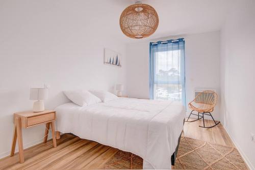 a white bedroom with a bed and a chair at Très belle appartement haut standing in Lacanau-Océan