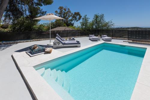 a swimming pool with chairs and an umbrella next to it at Erolidae Villas in Atsoupádhes