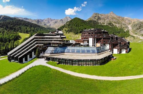 un bâtiment dans un champ avec des montagnes en arrière-plan dans l'établissement Blu Hotel Senales Zirm-Cristal, à Maso Corto