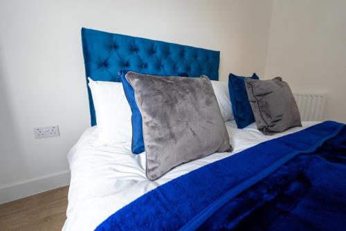 a bed with a blue headboard and pillows on it at Newly Built Spacious Apartment easily accessible to Luton Airport, Town centre and station in Luton