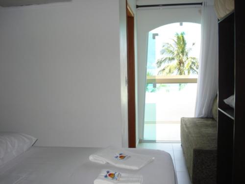 a room with a bed and a window with a palm tree at Valentina Praia Hotel in Barequeçaba