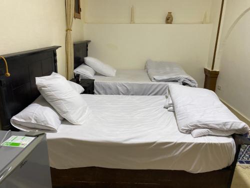 three beds in a room with white sheets and pillows at Pyramids Lounge Guest House in Cairo