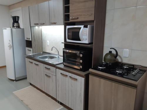 a kitchen with a microwave and a sink and a refrigerator at Apartamento Cantinho do Aconchego-Nova Petrópolis in Nova Petrópolis