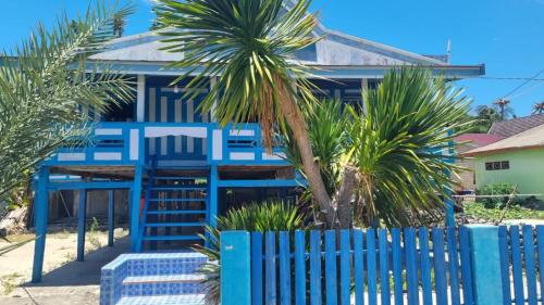 a blue fence in front of a house with palm trees at Home Stay Ramli in Bira