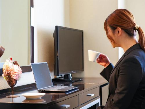 a woman drinking a cup of coffee in front of a computer at Fukui Hotel in Obihiro
