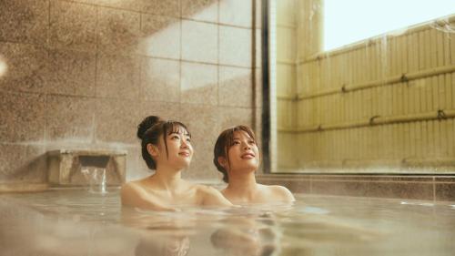 Dos mujeres sentadas en una bañera con agua en Hotel Sunmi Club Bekkan en Atami