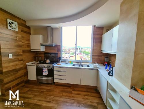 a kitchen with white cabinets and a sink and a window at Margarita Apartamentos in Cochabamba