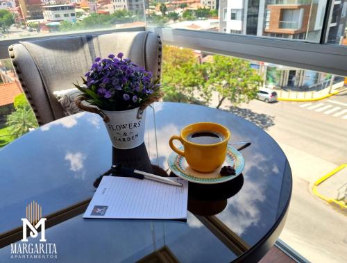 a table with a cup of coffee and a vase of purple flowers at Margarita Apartamentos in Cochabamba