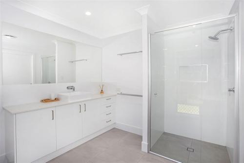 a white bathroom with a shower and a sink at Beautiful Beach House in the Heart of Town in Coolum Beach