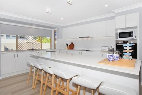 a kitchen with a large white counter and stools at Beautiful Beach House in the Heart of Town in Coolum Beach