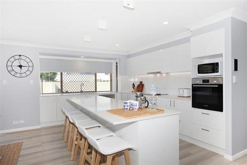 a white kitchen with a large island with stools at Beautiful Beach House in the Heart of Town in Coolum Beach