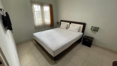 a bedroom with a bed with white sheets and a window at Planters Guest House in Yogyakarta