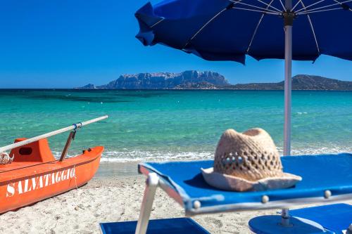 a straw hat sitting on a beach with a boat at Hotel Stefania Boutique Hotel by the Beach in Olbia