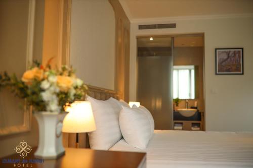 a bedroom with a bed with a vase of flowers on a table at L'amant de Hanoi Hotel - khách sạn Lamant de Hà Nội in Hanoi