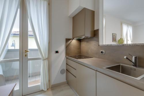 een keuken met witte kasten, een wastafel en een raam bij Residence Porto Letizia - Happy Rentals in Porlezza