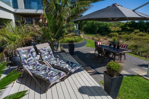 a patio with two chairs and a table with an umbrella at Absolute Beach in Mount Maunganui
