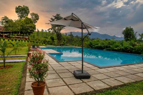 a swimming pool with an umbrella next to it at Pranavam Resort & Spa in Tariyod