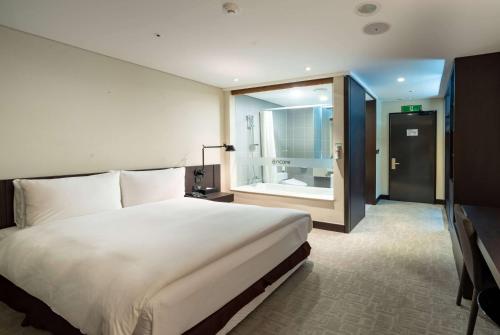 a bedroom with a large white bed and a bathroom at Ramada Encore by Wyndham CheonAn in Cheonan