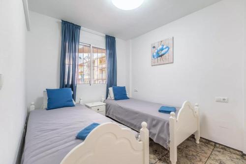 - 2 lits dans une chambre blanche avec des oreillers bleus dans l'établissement 040 Apartamento Norra, à Torrevieja