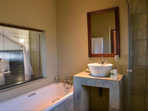 a bathroom with a sink and a tub and a mirror at Mjejane River Lodge in Hectorspruit