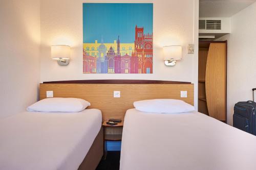 two beds in a room with a painting on the wall at Kyriad Direct Soissons in Soissons