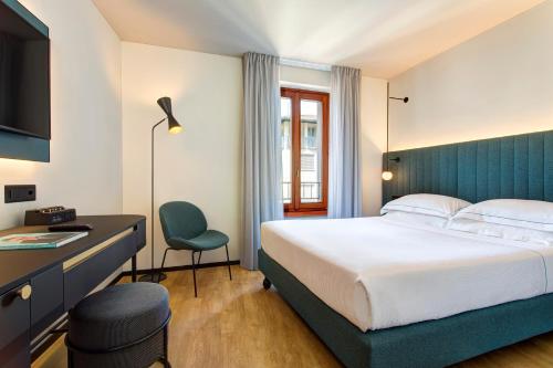 ルガノにあるLUGANODANTE - We like youのベッド、デスク、椅子が備わるホテルルームです。