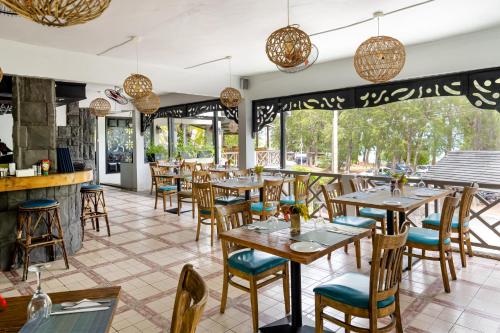 a restaurant with wooden tables and chairs and windows at Le Grand Bleu Hotel in Trou aux Biches