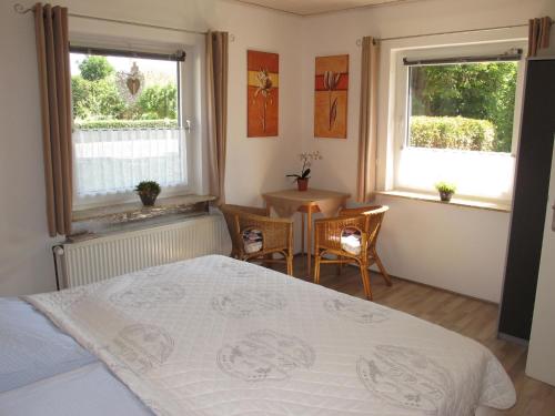 a bedroom with a bed and a table and two windows at Ferienhaus STICKLIESEL DITZ125 in Ditzum