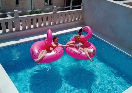 two girls riding on pink flamingos in a swimming pool at Apartment Making memories in Pučišća