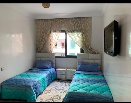 a bedroom with two beds and a tv and a window at Residence miramar in Mohammedia