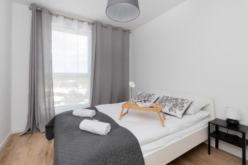 a white bedroom with a bed with a table and a window at Osiedle Latarników Apartment Gdańsk by Renters in Gdańsk