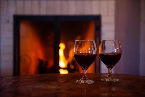 two glasses of wine sitting on a table in front of a fireplace at Pousada Alpes da Mantiqueira in Monte Verde
