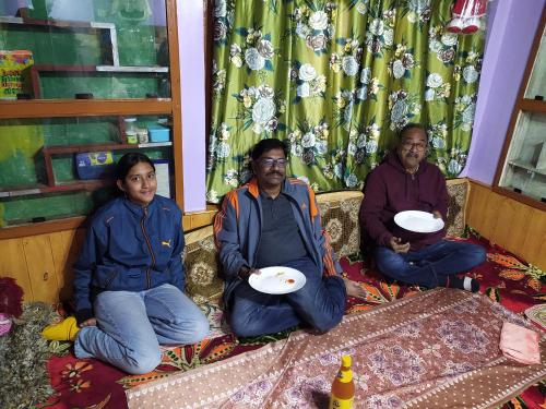 Mir guest house في باهالجام: مجموعة من ثلاثة أشخاص يجلسون على أريكة يحملون الأطباق