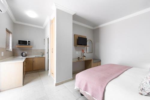 a white bedroom with a bed and a kitchen at Adato Guesthouse in Potchefstroom